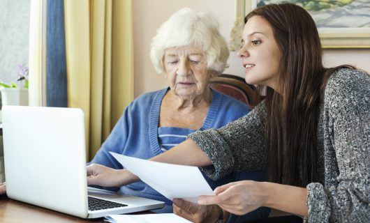 Grandmother and granddaughter with document using laptop at home